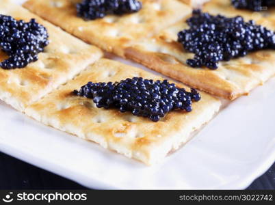 Black caviar over crackers, white tray, horizontal image