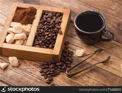 Black ceramic cup of fresh raw organic coffee with beans and ground powder with cane sugar in vintage box on wooden background.