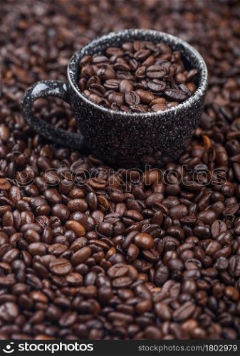 Black ceramic cup with fresh raw coffee beans inside beans background. Macro