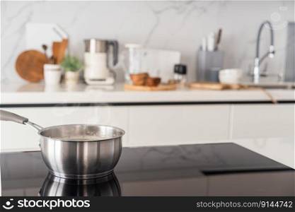 Black ceramic induction stove and saucepan on top. Contemporary home with modern interior, built in kitchen appliance and white tile on wall with copy space. Stove and saucepan on top.