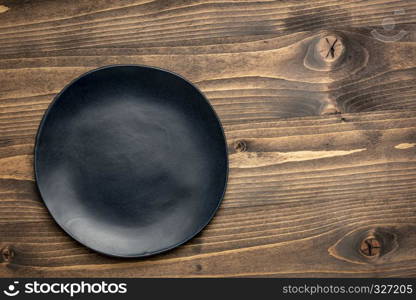 black ceramic plate with an irregular edge on a grained wood with a copy space