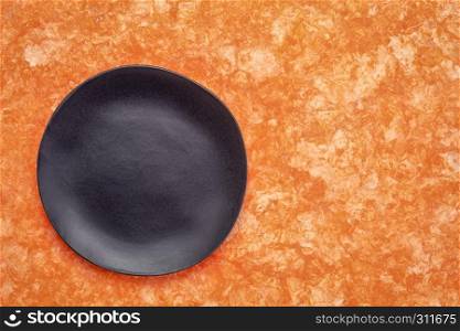 black ceramic plate with an irregular edge on an orange amate bark paper with a copy space