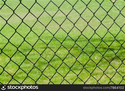 Black chain link fence against empty green grass field.