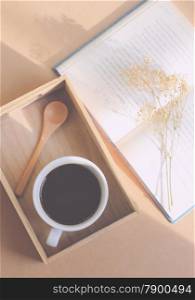 Black coffee and spoon on wooden tray with book, retro filter effect