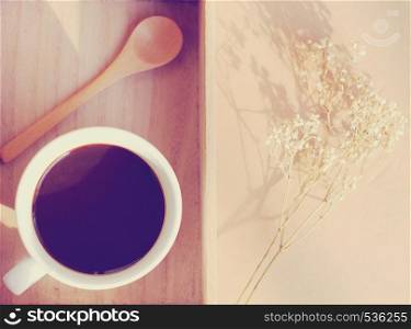 Black coffee and spoon on wooden tray with dried flower, retro filter effect