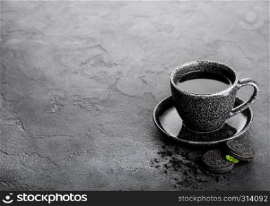 Black coffee cup with saucer and black sandwich cookies on black stone kitchen table background. Breakfast snack