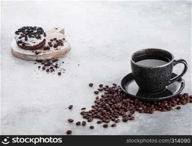 Black coffee cup with saucer and doughnut with black cookies on stone kitchen table background. Space for text.