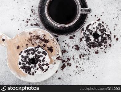 Black coffee cup with saucer and doughnuts with black cookies on stone kitchen table background. Top view