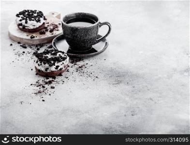 Black coffee cup with saucer and doughnuts with black cookies on stone kitchen table background. Space for text.