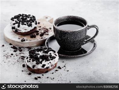 Black coffee cup with saucer and doughnuts with black cookies on stone kitchen table background.