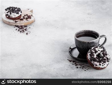 Black coffee cup with saucer and doughnuts with black cookies on stone kitchen table background. Space for text.