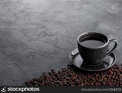 Black coffee cup with saucer and fresh coffee beans on black stone kitchen table background.