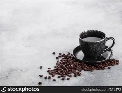 Black coffee cup with saucer and fresh coffee beans on stone kitchen table background.