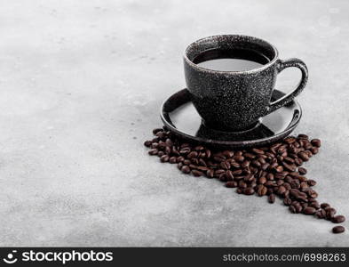 Black coffee cup with saucer and fresh coffee beans on stone kitchen table background.