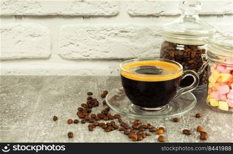 Black coffee espresso in a glass with cream and marshmallows in a glass jar. Coffee beans on gray and white brick wall surface with copy space. Black coffee espresso in a glass cup