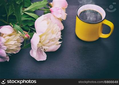 Black coffee in a yellow mug and a bouquet of white peonies on a black background