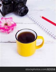 black coffee in a yellow round cup on a white wooden table, top view