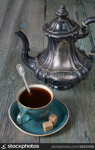 Black coffee in blue vintage cup and antique silver coffee pot on a old dark wooden boards