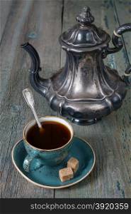 Black coffee in blue vintage cup and antique silver coffee pot on a old dark wooden boards