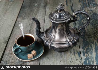 Black coffee in blue vintage cup and beautiful antique silver coffee pot on an old dark wooden boards