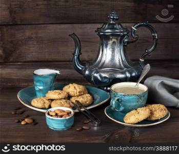 Black coffee in blue vintage cup, cookies and antique silver coffee pot on a old dark wooden boards