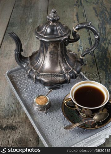 Black coffee in vintage cup and antique silver coffee pot on a old dark wooden boards