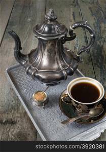 Black coffee in vintage cup and antique silver coffee pot on a old dark wooden boards