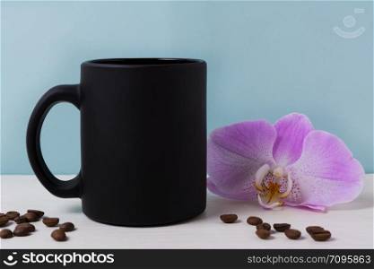 Black coffee mug mockup with purple orchid and coffee beans. Empty mug mock up for brand promotion.