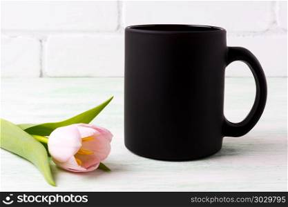 Black coffee mug mockup with tender pink tulip flower. Empty mug mock up for brand promotion.. Black coffee mug mockup with pink tulip