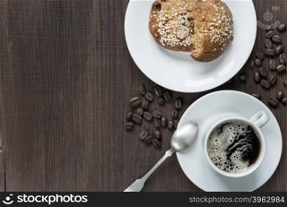 Black coffee with froth in white porcelain cup, coffee beans and oatmeal cookies on a dark wooden background, top view