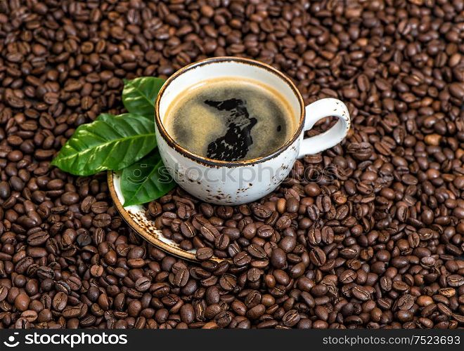 Black coffee with green leaves on caffee beans background. Food und drinks