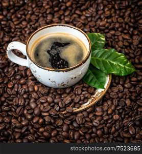 Black coffee with green leaves on caffee beans background. Vintage style toned picture