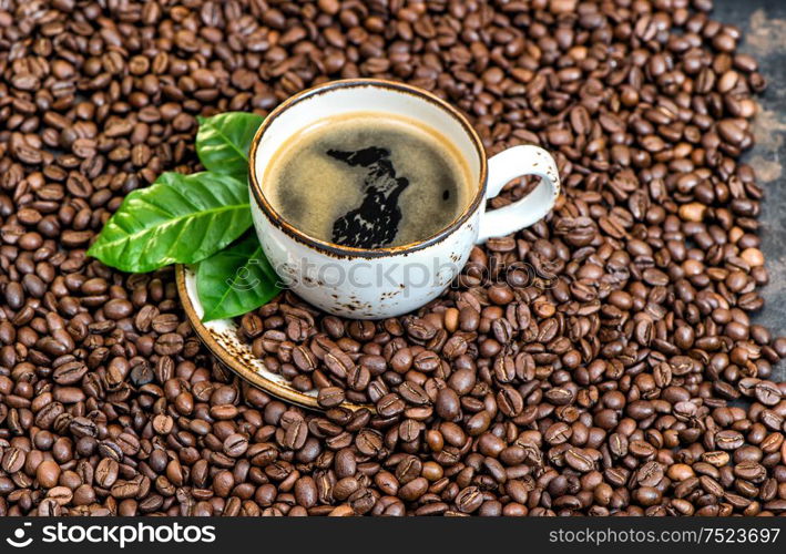 Black coffee with green leaves on coffee beans background. Food und drinks