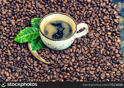 Black coffee with green leaves on coffee beans background. Vintage style toned picture