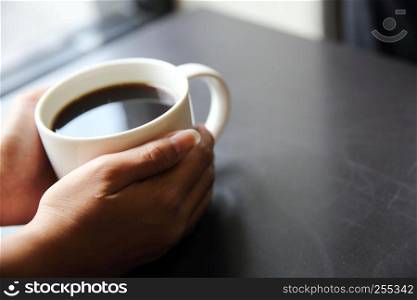 Black coffee with hand on wood background in coffee shop