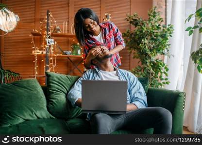 Black couple with laptop having fun on sofa at home. Happy african love couple leisures in their house, cheerful family relaxing at home. Black couple with laptop having fun on sofa