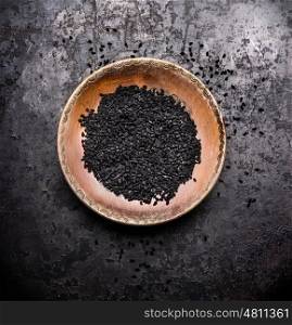 Black cumin seeds in rustic bowl on dark vintage background, top view. Nigella sativa seeds