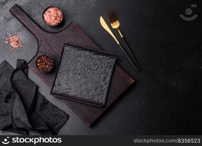 Black cutlery on a concrete dark table. Dining table preparation. Empty black plate over dark stone background with free space. Top view