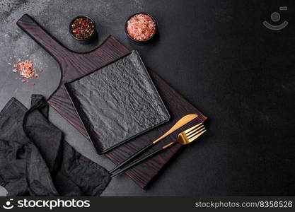 Black cutlery on a concrete dark table. Dining table preparation. Empty black plate over dark stone background with free space. Top view