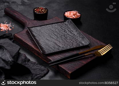 Black cutlery on a concrete dark table. Dining table preparation. Empty black plate over dark stone background with free space. Top view