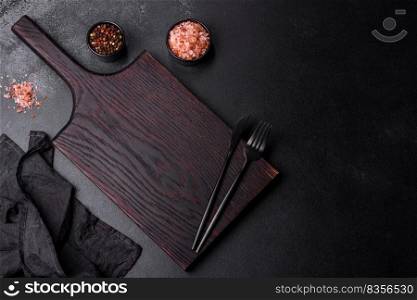 Black cutlery on a concrete dark table. Dining table preparation. Empty black plate over dark stone background with free space. Top view