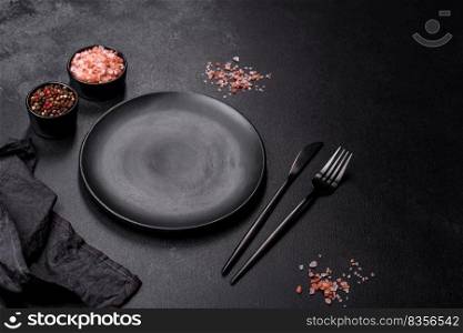 Black cutlery on a concrete dark table. Dining table preparation. Empty black plate over dark stone background with free space. Top view
