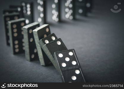 Black dominoes chain on a dark table background. Domino effect concept. Black dominoes chain on dark table background