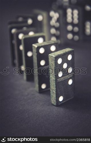 Black dominoes chain on a dark table background. Domino effect concept. Black dominoes chain on dark table background