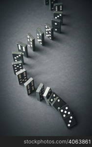 Black dominoes chain on a dark table background. Domino effect concept. Black dominoes chain on dark table background