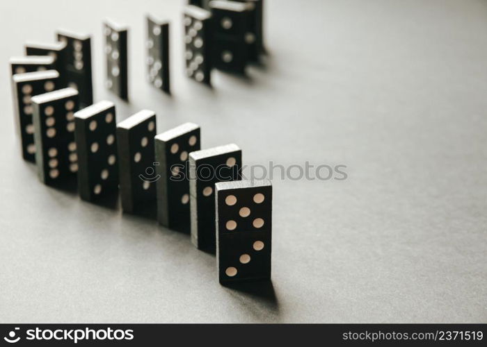 Black dominoes chain on a white table background. Domino effect concept. Black dominoes chain on white table background