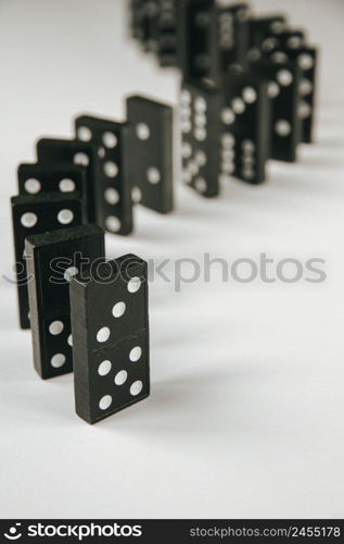 Black dominoes chain on a white table background. Domino effect concept. Black dominoes chain on white table background
