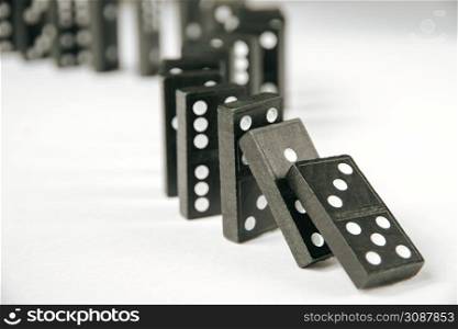 Black dominoes chain on a white table background. Domino effect concept. Black dominoes chain on white table background