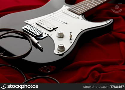 Black electric guitar, red background, nobody. String musical instrument, electro sound, electronic music. Black electric guitar, red background, nobody