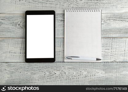 black electronic tablet and paper notebook on vintage shabby white wooden background. the view from the top. flat lay